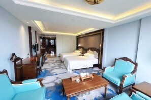 Una habitación de hotel con cama, dos mesitas de noche, una mesa de centro y una zona de estar con sillas.
