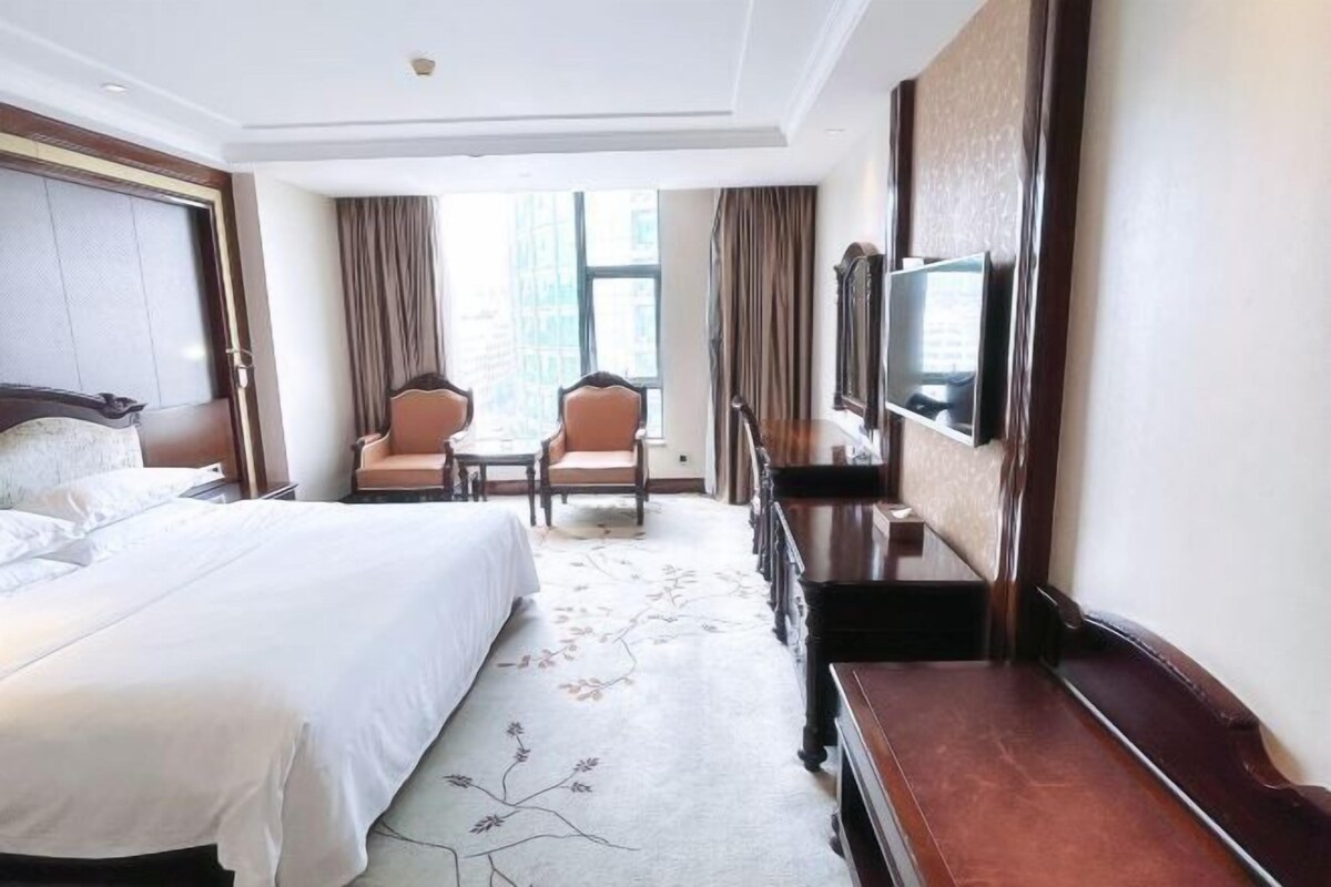 Habitación de hotel con una cama grande, un escritorio, dos sillas, un televisor y vistas de la ciudad.