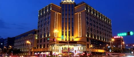 Ein mehrgeschossiges Hotel mit einem markanten, zentralen Turm, beleuchteter Beschilderung und einer belebten Straße im Vordergrund.