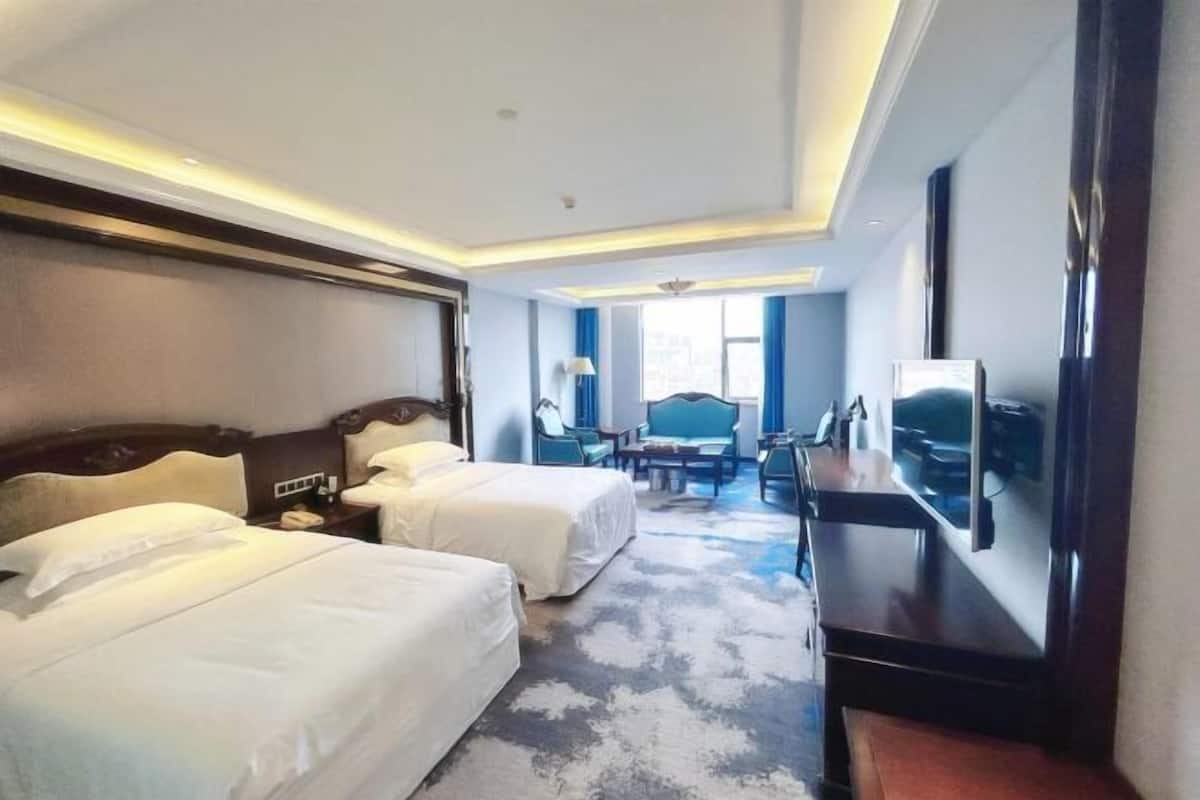 A hotel room with two beds, a desk, a chair, a TV, and a large window.