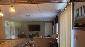 A bar area with stools, a wooden counter, and a television mounted on the wall. - Sacandaga Lake Adirondack Escape (Gloversville)
