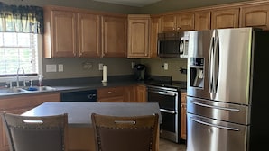 A kitchen with wooden cabinets, a stainless steel refrigerator, a microwave, and a sink. - Sacandaga Lake Adirondack Escape (Gloversville)