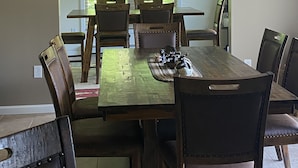 A dining area with a large wooden table, multiple chairs, and a chandelier with antler decorations. - Sacandaga Lake Adirondack Escape (Gloversville)