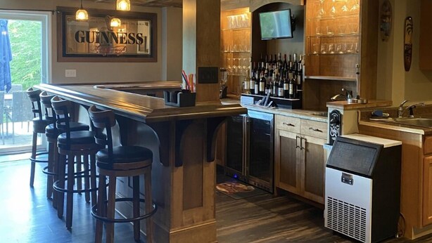 A bar area with a Guinness sign, bar stools, a TV, and a wine cooler. - Sacandaga Lake Adirondack Escape (Gloversville)