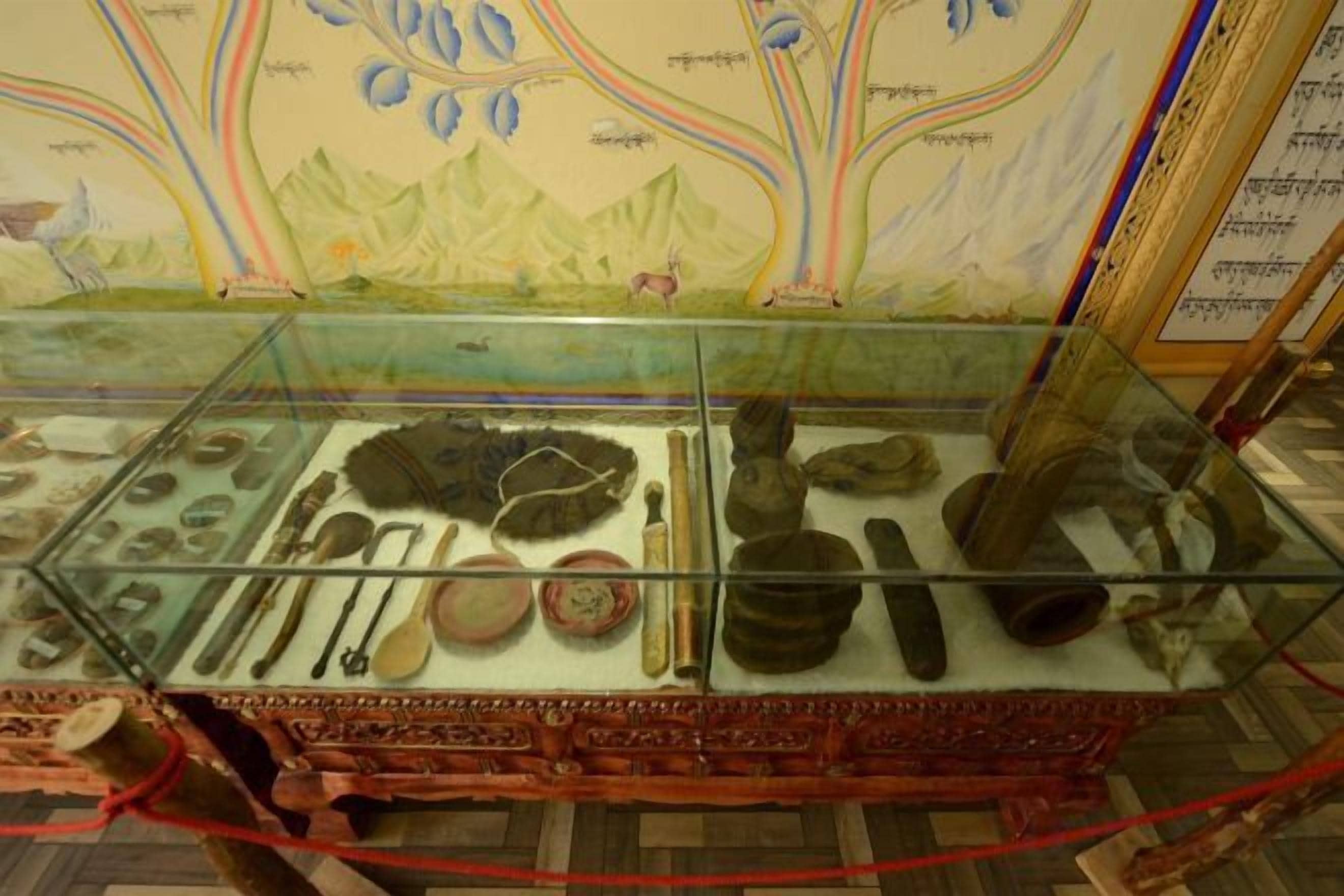 Una vitrina de museo exhibe diversos artefactos, como cerámica y herramientas, frente a un mural colorido.