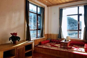 Quarto com um banco de madeira, uma mesa pequena e uma janela com cortinas.