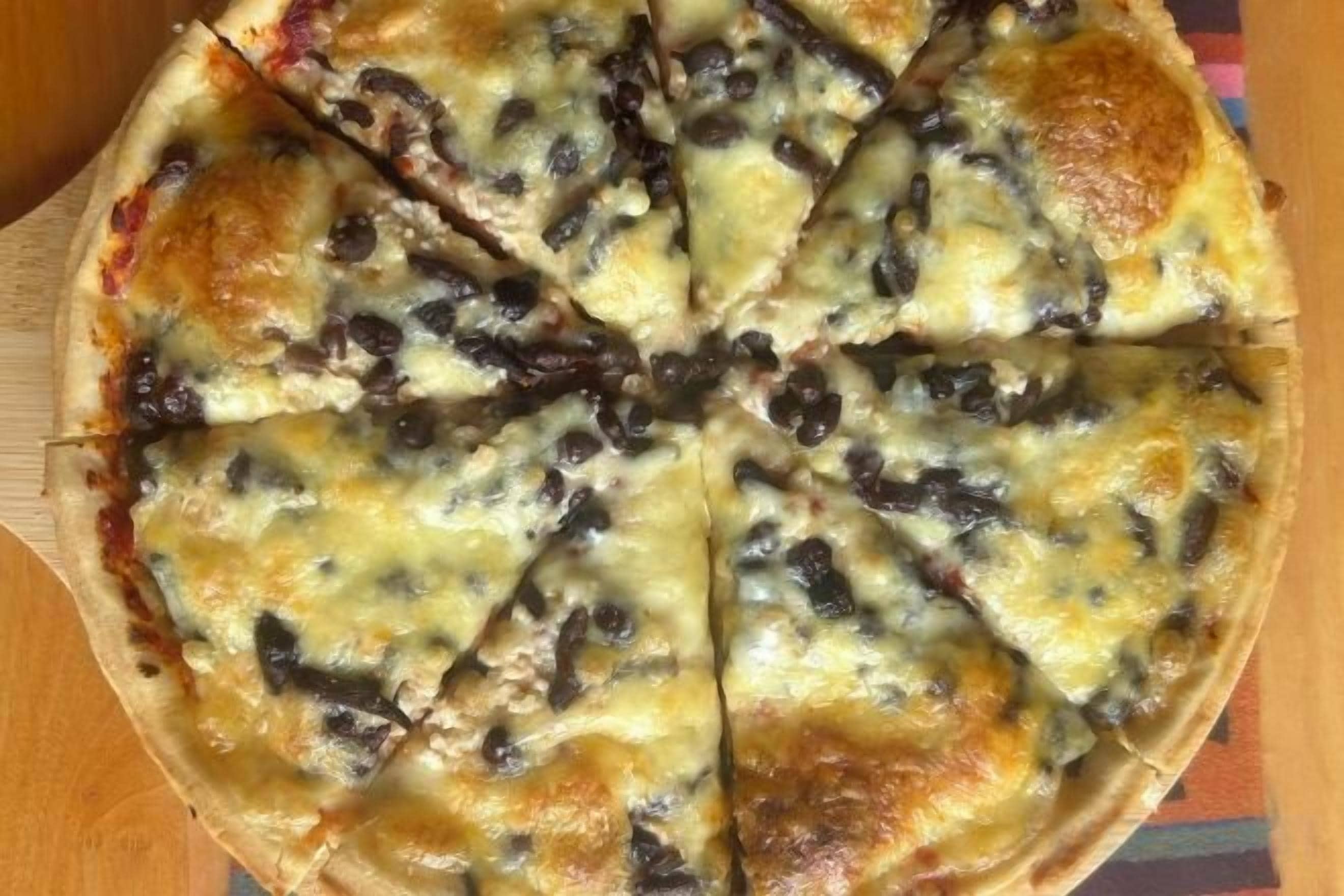 A pizza with black olives and melted cheese on a wooden board.
