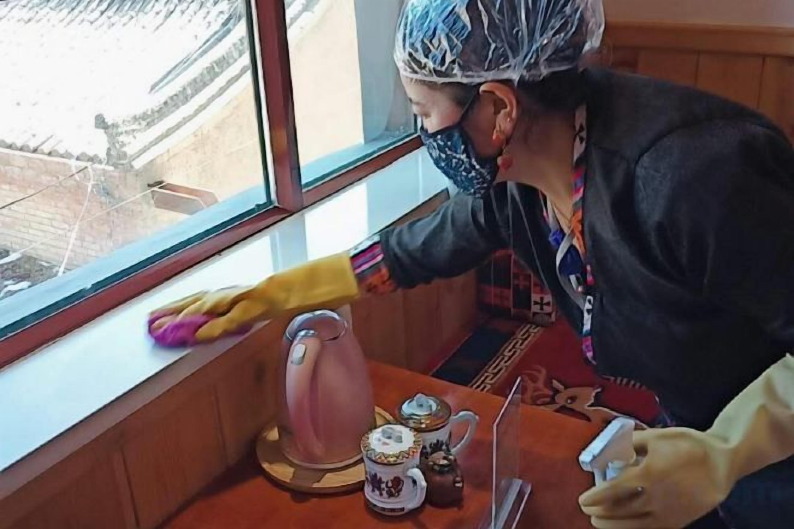 A person cleaning a window with a cloth, a kettle, and teacups on a table.