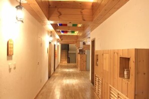 Un couloir en bois, avec un escalier au fond, des lambris en bois sur les murs et un luminaire sur le côté gauche.