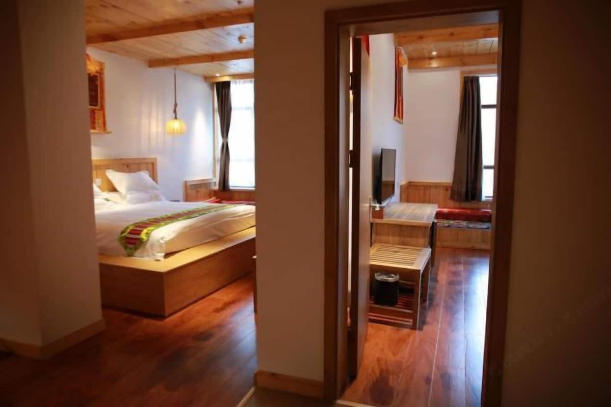 A bedroom with a wooden bed, a bedside table, a TV, and a window with curtains.