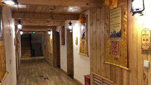A wooden interior hallway with a staircase at the end, wooden walls, and several wall-mounted light fixtures.