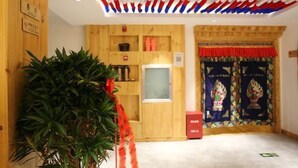 A room with wooden walls, a large potted plant, a shelf with kitchen items, and a door with a colorful curtain.