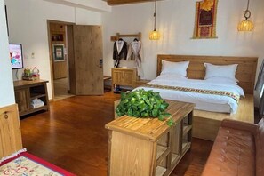 Een slaapkamer met een houten bed, een nachtkastje, een kleine plant, een houten bankje, een rood-wit gestreept vloerkleed en een bruine leren bank.