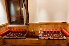 Un banco de madera con cojines rojos y un tapete estampado, ubicado cerca de una ventana con cortinas.