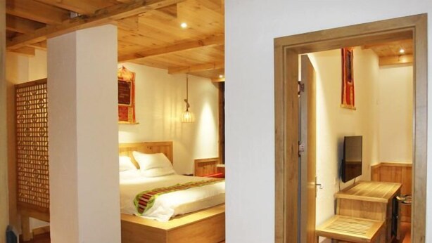 A hotel room with a wooden bed, a small desk, a TV, and a wooden floor.