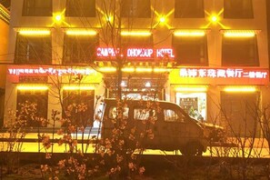Un bâtiment avec une enseigne lumineuse, un véhicule garé devant et un arbre au premier plan.