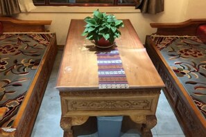Une table en bois ornée d’un chemin de table à motifs, d’une plante en pot et de sculptures complexes sur le pied de la table.