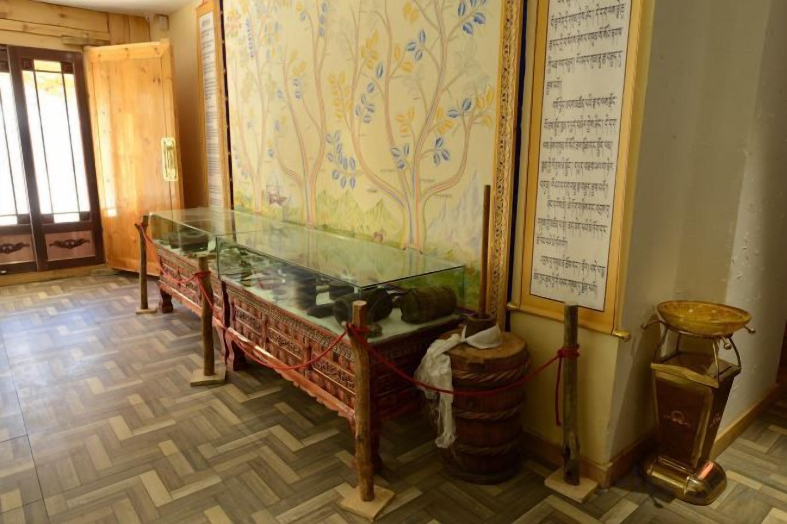 Una habitación con una vitrina de vidrio, una mesa de madera tradicional y una pared grande con un mural de un árbol.