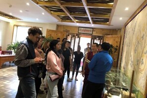 A group of people in a lobby with a glass display case and a wooden ceiling. - Sangpei Dongzhu Inn (Xiahe)