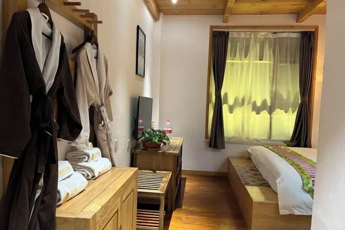 A bedroom with a bed, a wooden bench, a small table with a plant, and a window with curtains.