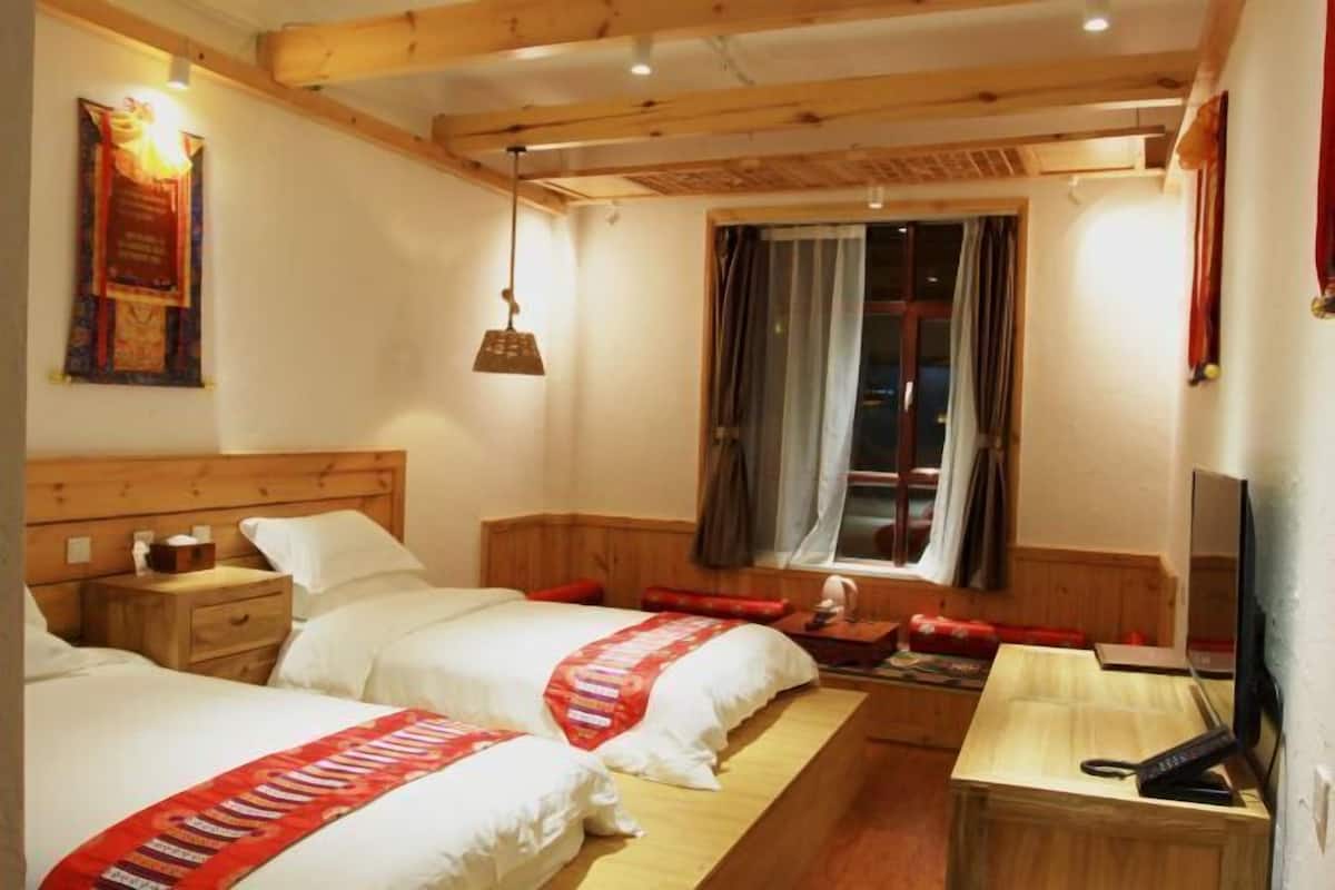 A hotel room with two beds, wooden headboard, bedside tables, a desk, a chair, a TV, and a window with curtains.