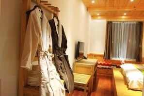 Quarto com cama de madeira, mesa de cabeceira, uma cadeira e um guarda-roupa com roupas penduradas.