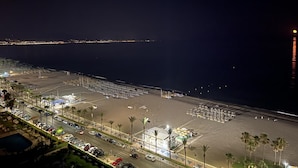 A beachside hotel with a parking area, beach umbrellas, and a view of the ocean.