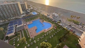 A resort with a swimming pool, a tennis court, and a view of the ocean at sunset.