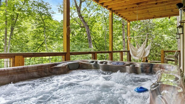 A hot tub with a wooden deck, surrounded by trees.