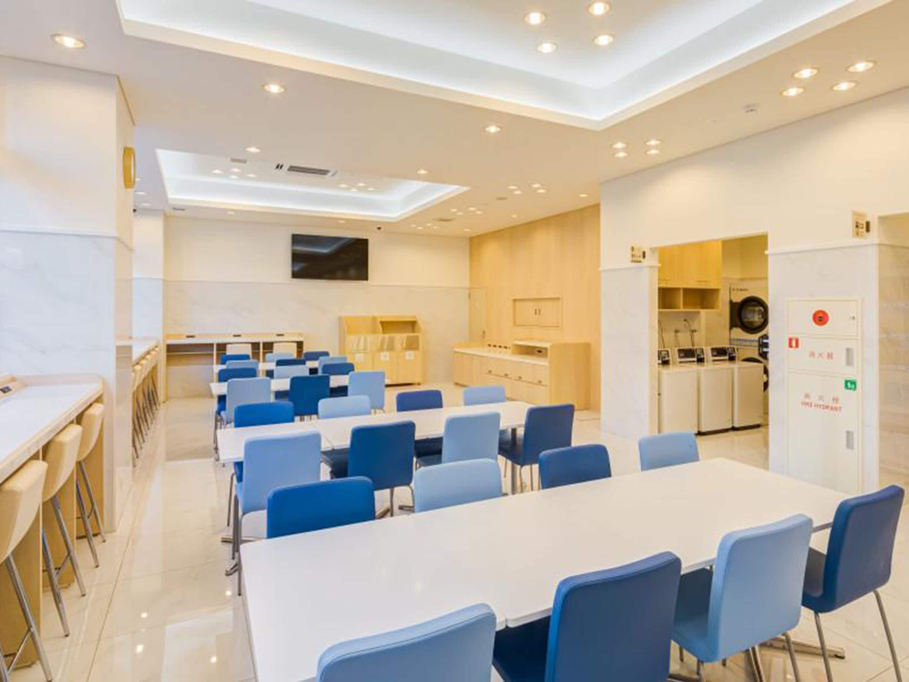 Una sala conferenze moderna con un lungo tavolo e sedie blu, un angolo cottura con elettrodomestici e un idrante visibile.
