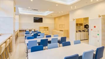 Una sala de conferencias moderna con una mesa larga y sillas azules, una zona de cocina con electrodomésticos y un hidrante visible.