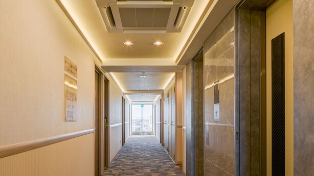 Een hotelgang met een zwart-wit geruit tapijt, deuren aan beide zijden en een lift aan de rechterkant.