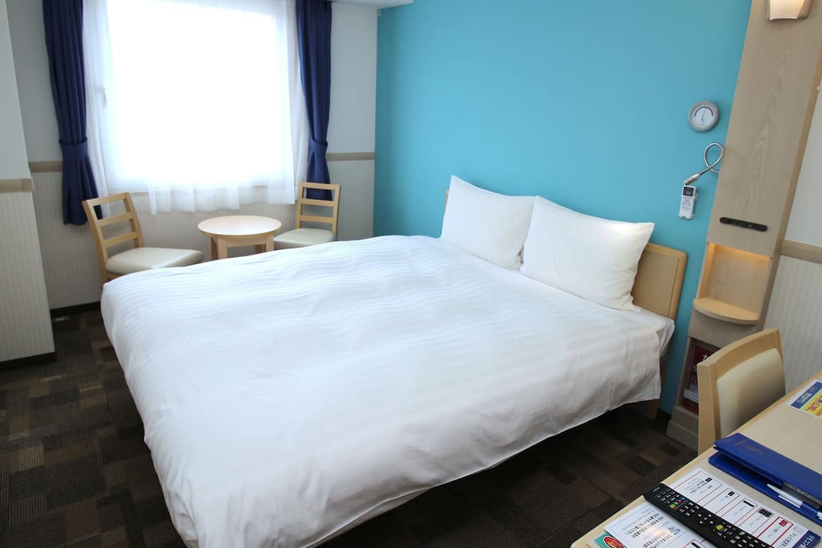 Una habitació d'hotel amb un llit gran, dues cadires, una taula petita i un rellotge a la paret.
