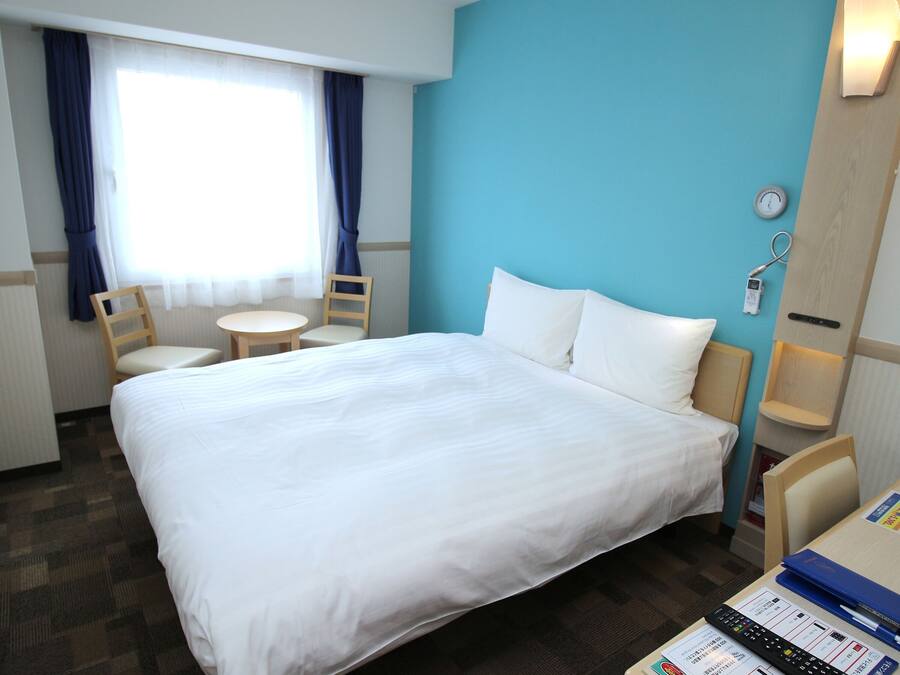A hotel room with a large bed, two chairs, a small table, and a clock on the wall.