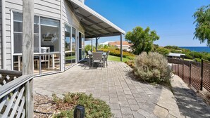 Una veranda coperta con mobili da esterno, vista sull'oceano e un'area giardino.