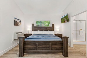 Une chambre à coucher avec un lit en bois, des murs blancs, une fenêtre et un téléviseur fixé au mur.
