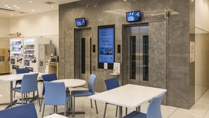 A modern interior with a vending machine, a digital information board, and a seating area with tables and chairs. - Toyoko Inn Kita-asaka-eki Nishi-guchi (Asaka)