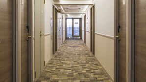 A hotel hallway with carpeted floors, doors on both sides, and a view of the city through the open door at the end. - Toyoko Inn Kita-asaka-eki Nishi-guchi (Asaka)
