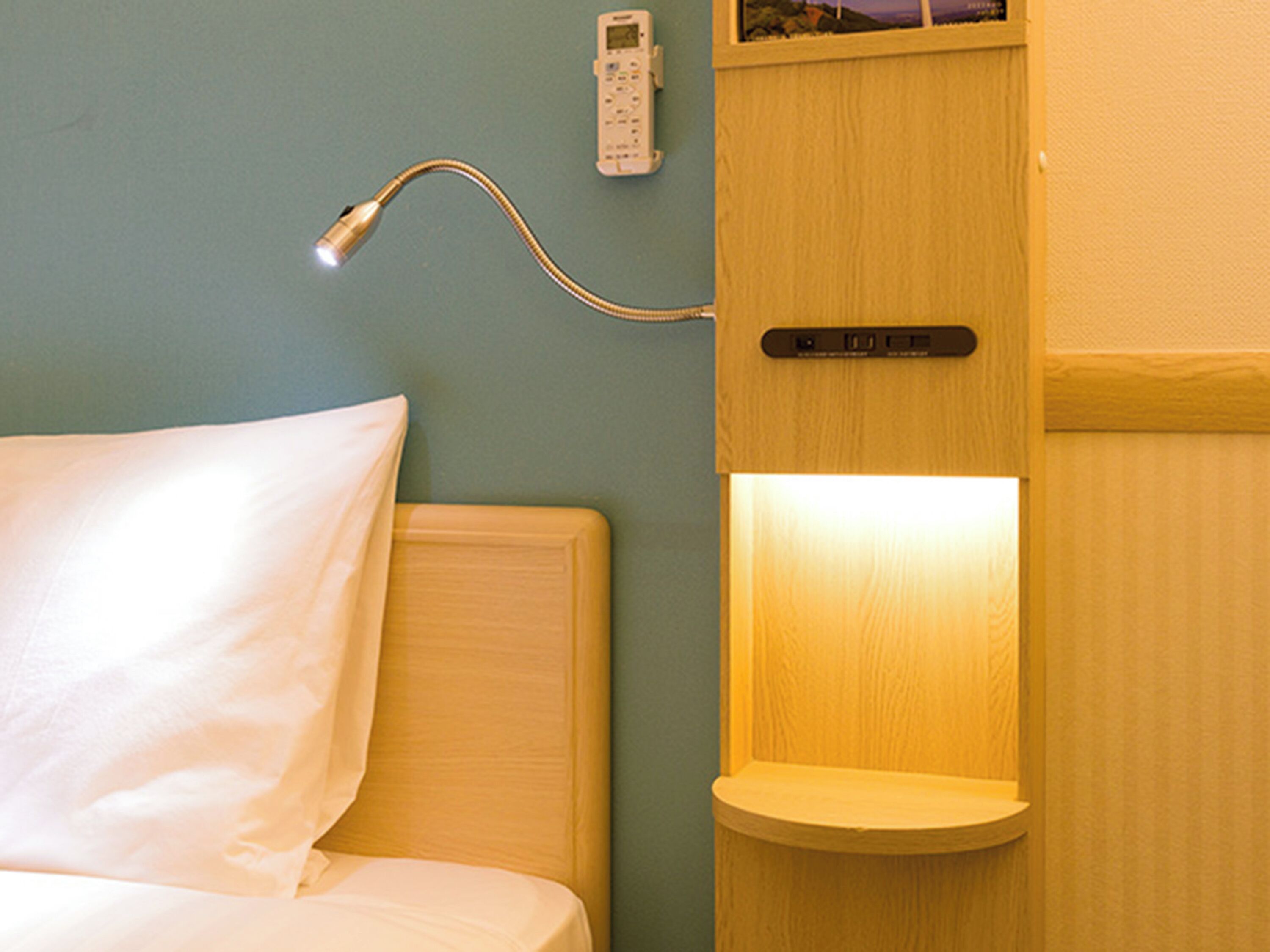 Habitación de hotel con una cama, una mesita de noche, un teléfono en la pared y un estante con luz.