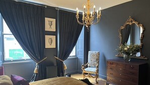A bedroom with a large bed, a chandelier, a dresser, a chair, and a mirror. - Luxury flat 2 mins from tram stop in the 4th coolest neighbourhood in the world! (Edinburgh)