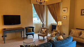 A living room with a blue sofa, two armchairs, a coffee table, a TV, and a chandelier. - Luxury flat 2 mins from tram stop in the 4th coolest neighbourhood in the world! (Edinburgh)