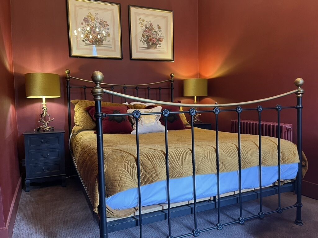 A bedroom with a four-poster bed, two bedside tables with lamps, and two framed floral artworks on the wall.