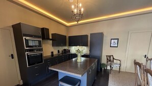 A modern kitchen with dark cabinetry, a central island, and a chandelier. - Luxury flat 2 mins from tram stop in the 4th coolest neighbourhood in the world! (Edinburgh)