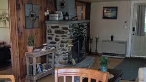 Una sala de estar acogedora con chimenea de piedra, muebles de madera y una mesa de comedor con un mantel tejido.