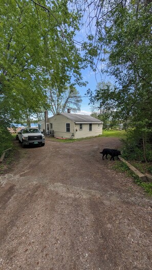 A single-story house with a gravel driveway, a parked truck, and a dog in the yard.