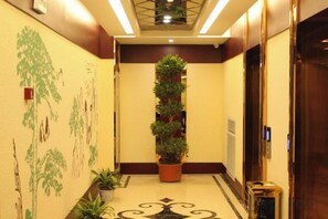 Un pasillo de hotel con una planta en maceta en el centro, suelo estampado y una puerta a la derecha.