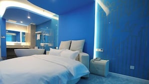 A modern bedroom with a large bed, a nightstand, a bathroom with a bathtub, and a blue wall with a floral pattern. - Jinlihua Hotel (Zhangjiagang)