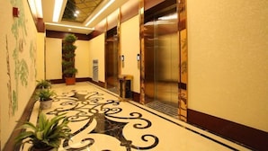 A hotel lobby with a marble floor, potted plants, and elevators. - Jinlihua Hotel (Zhangjiagang)