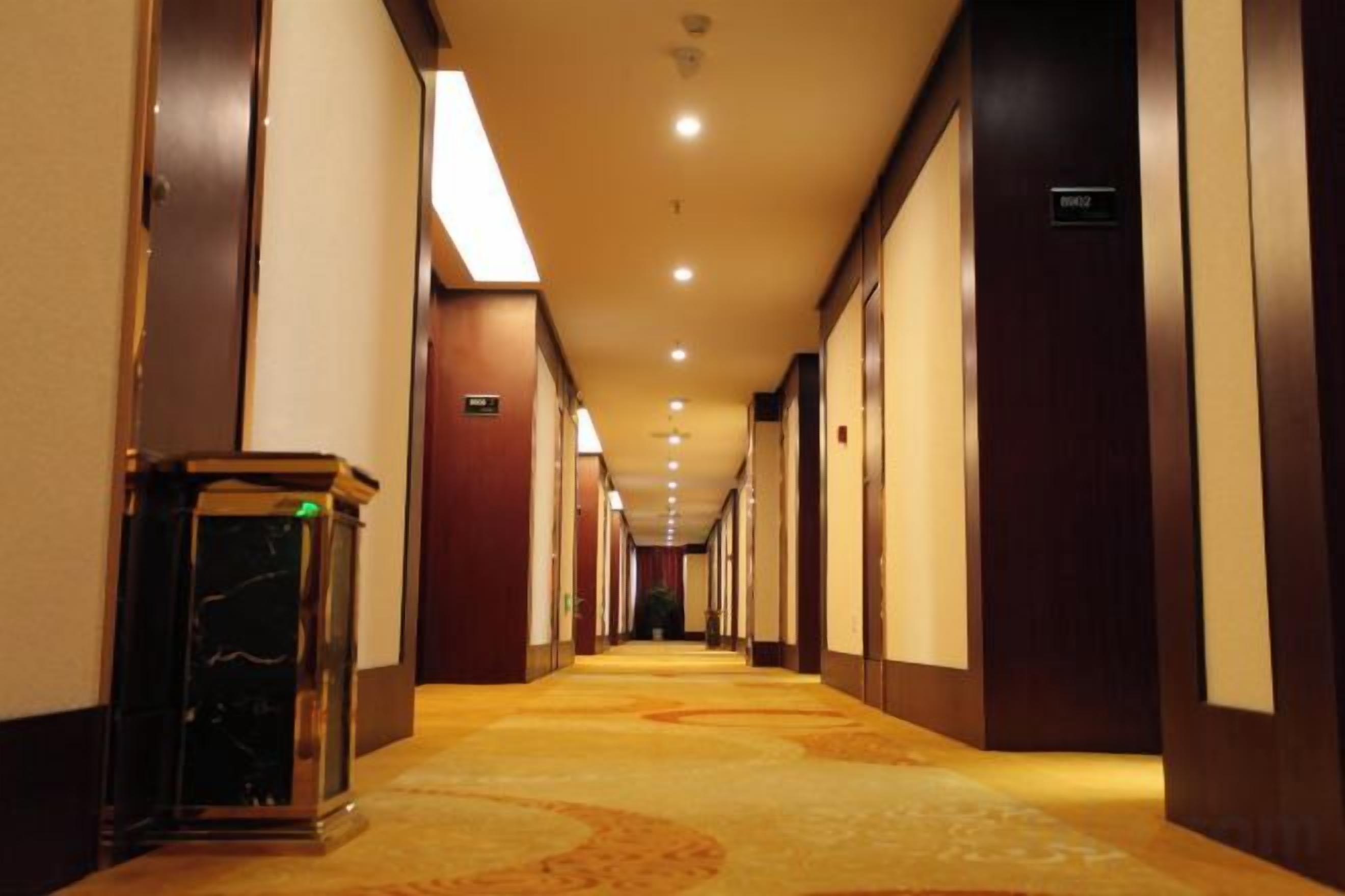 Un pasillo de hotel con piso alfombrado, puertas a la derecha y un cubo de basura a la izquierda.