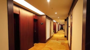 A hotel hallway with wooden doors, carpeted floors, and overhead lighting. - Jinlihua Hotel (Zhangjiagang)